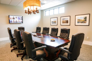a long wooden conference room table with 10 chairs, a tv on the far wall, and windows and pictures on the side wall.